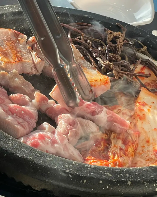 돌판 위에 구워지는 삼겹살, 김치, 고사리