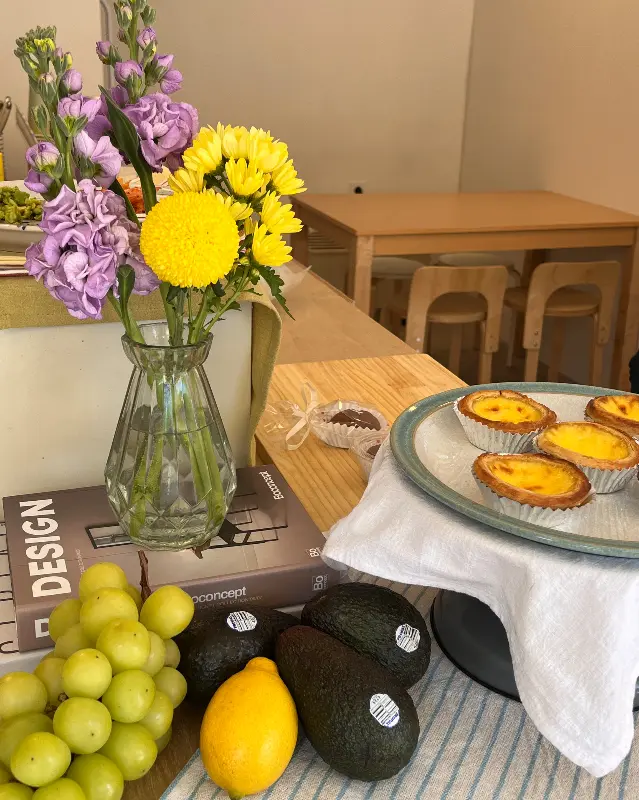 테이블 위에 놓인 에그 타르트와 시금치 파이, 과일, 꽃병