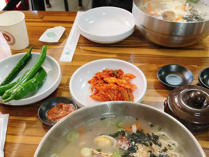 테이블 위에 놓인 바지락 칼국수, 김치, 고추, 다진 양념