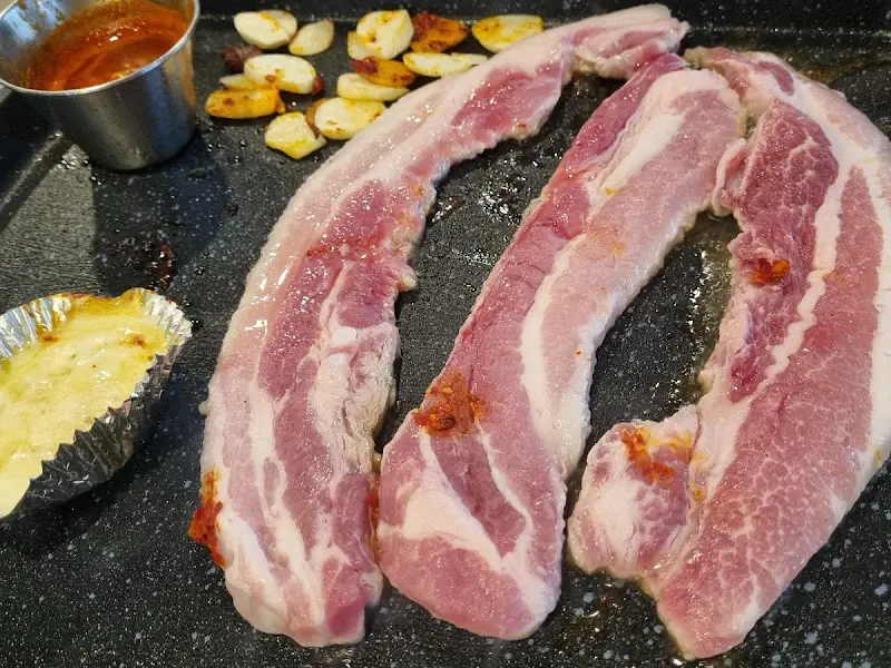 불판 위에 익어가는 삼겹살, 김치, 마늘, 치즈