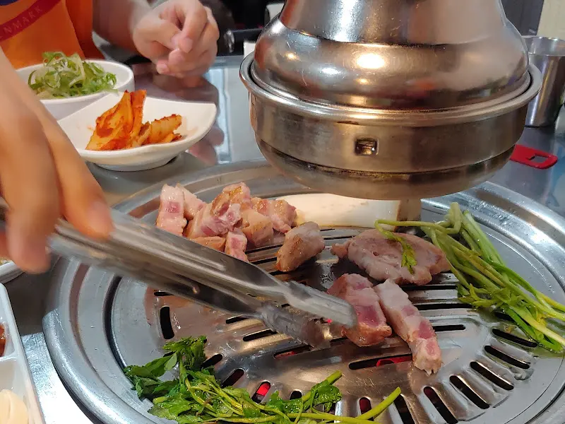 불판 위에서 지글거리는 흑돼지 삼겹살과 미나리