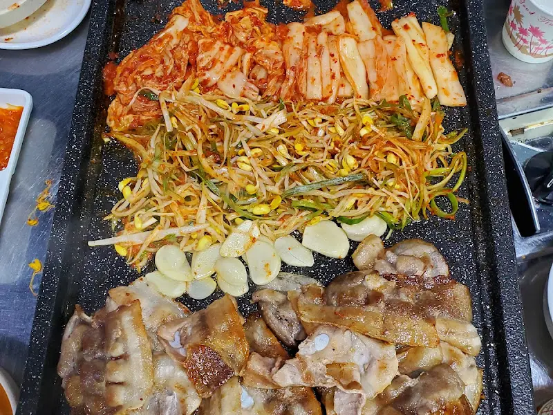 불판에 구워진 삼겹살과 콩나물, 김치의 모습