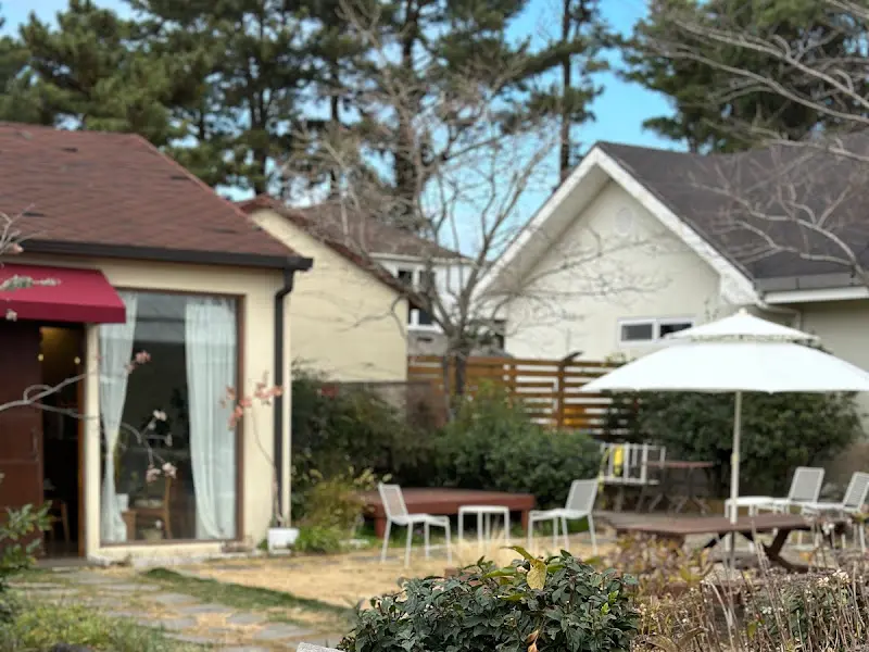 카페 외부 전경: 붉은색 차양이 드리워진 입구와 아기자기한 정원이 조화롭다.