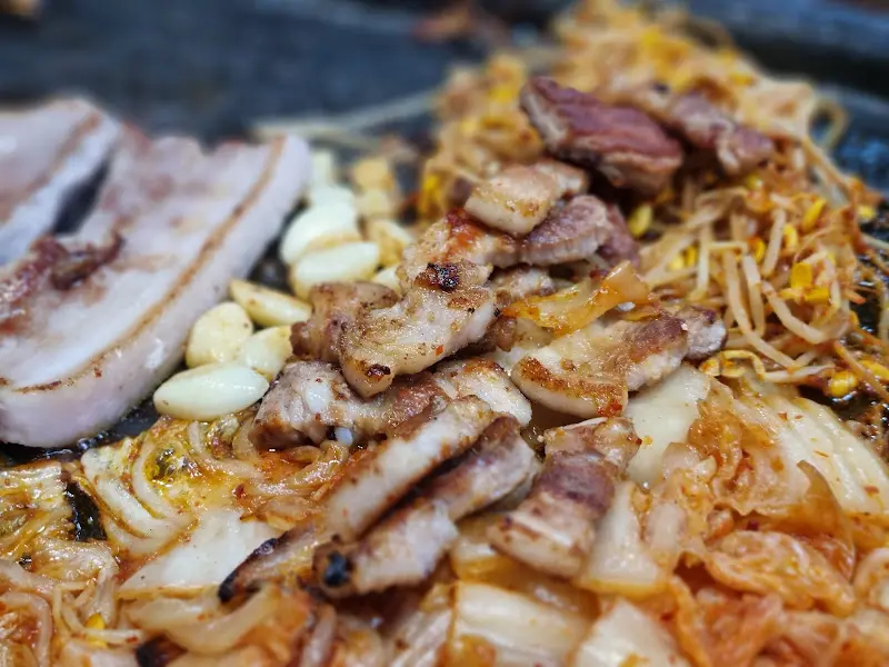 불판 위에서 구워지는 삼겹살, 김치, 콩나물무침