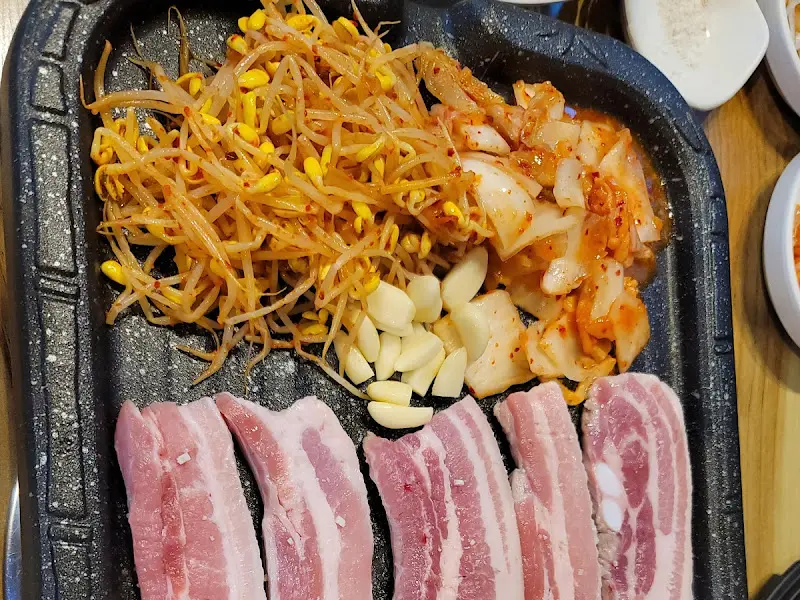 불판 위에 올려진 삼겹살과 김치, 콩나물