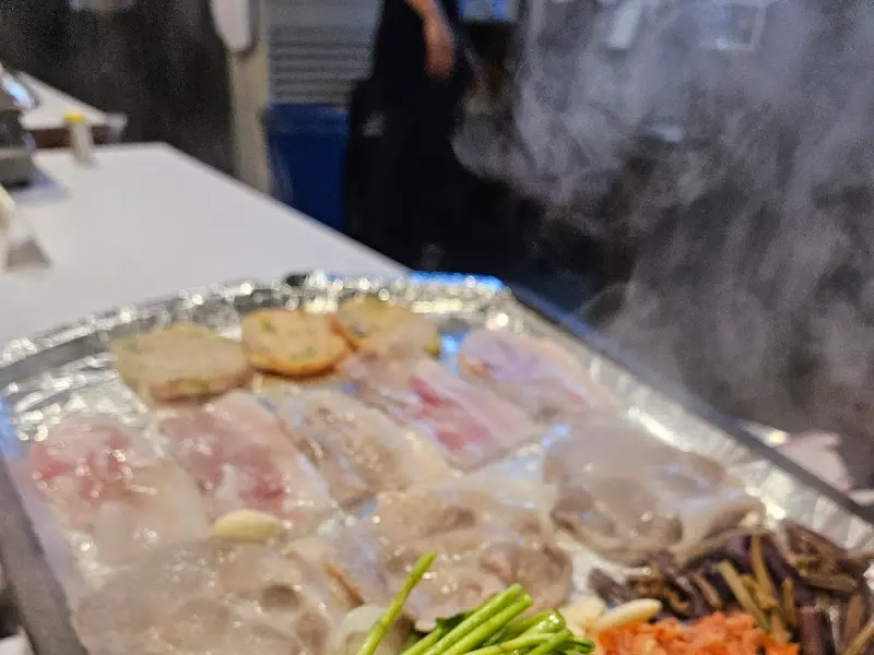 불판 위에서 연기를 내며 익어가는 냉동 삼겹살