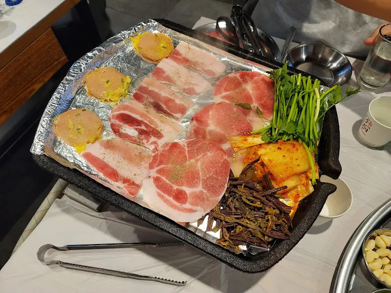 불판 위에서 익어가는 냉동 삼겹살과 김치, 미나리, 고사리