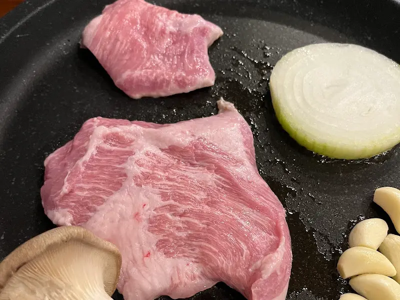 불판 위에서 익어가는 약돌돼지 삼겹살과 채소들