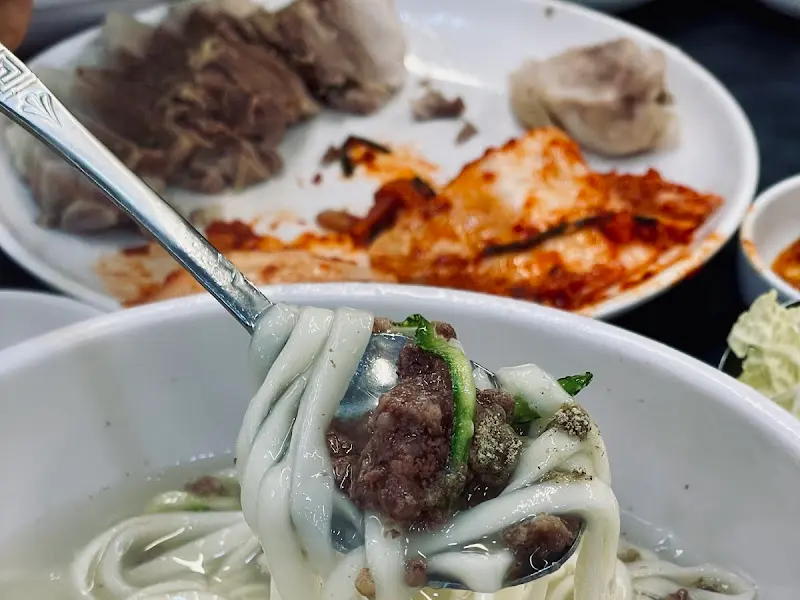 수저 위에 올려진 칼국수와 고기 고명