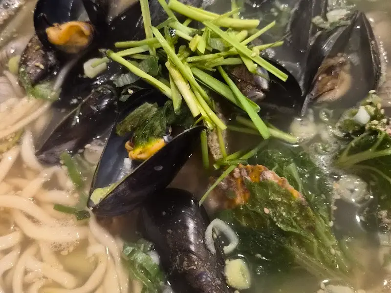 해물칼국수의 클로즈업 사진. 홍합과 미나리가 듬뿍 올려져 있다.