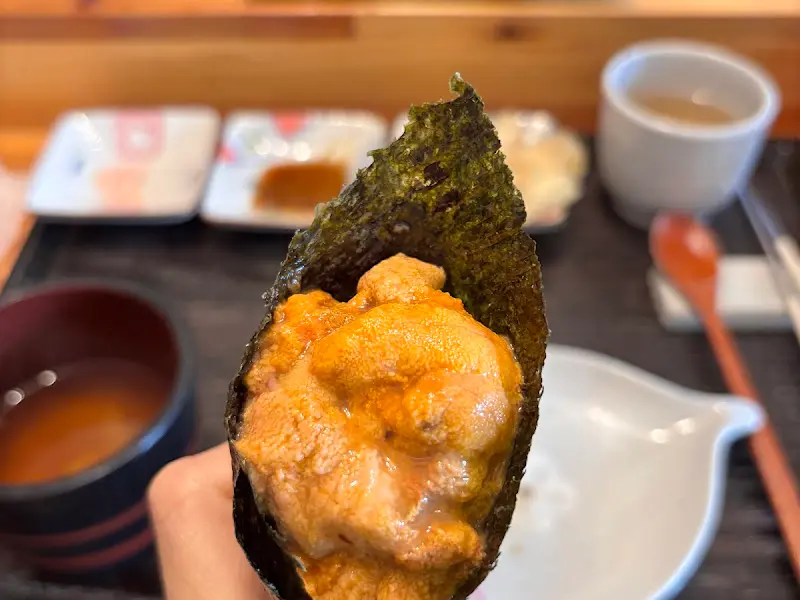 손에 들린 김 마끼 안에 주황색 성게가 가득 차 있는 모습