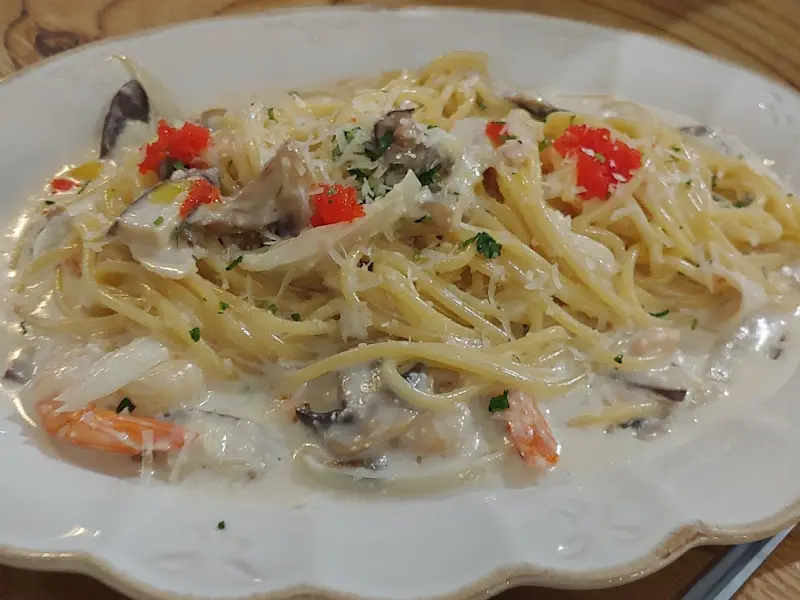 크림 파스타 위에 붉은 색의 명란이 얹혀져 있고, 초록색 채소가 장식되어 있다.