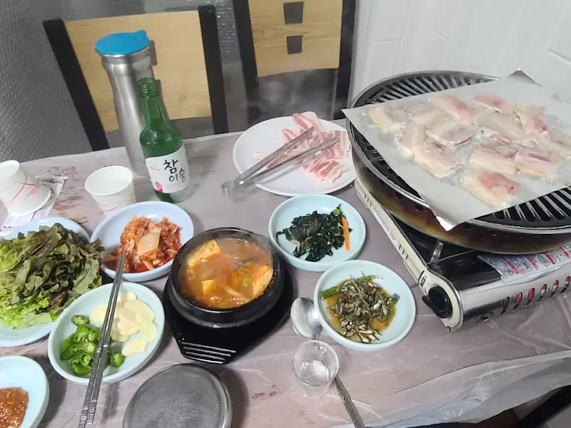 불판 위의 냉동 삼겹살과 곁들임 반찬