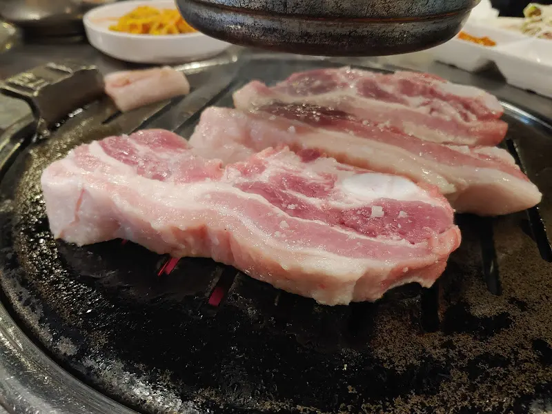 두툼한 삼겹살이 불판 위에서 지글지글 익어가는 모습