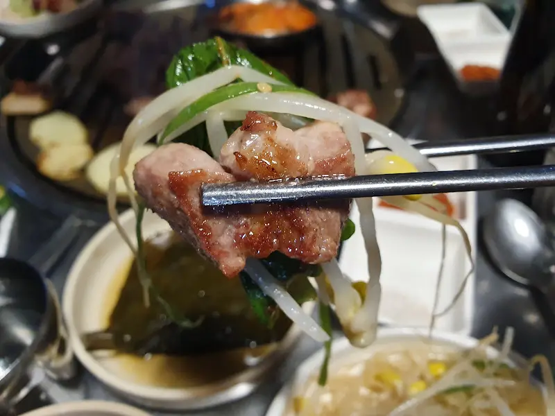 잘 익은 목살을 깻잎 무침과 함께 젓가락으로 집어 올린 모습