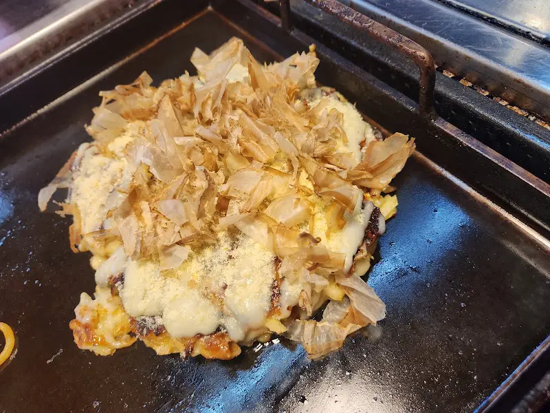 철판 위에 놓인 오코노미야끼 위에 가쓰오부시가 흩뿌려진 모습