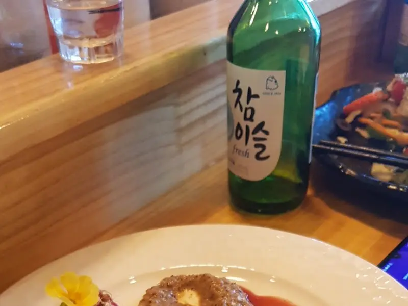 테이블 위에 놓인 접시에는 먹음직스러운 갈비찜이 담겨 있고, 그 옆에는 참이슬 병이 놓여 있다.