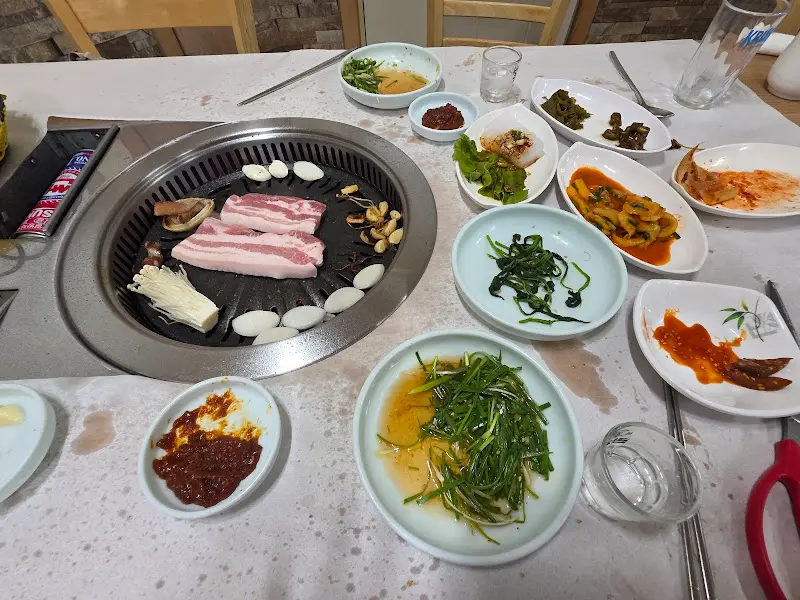 다채로운 밑반찬과 삼겹살이 구워지고 있는 테이블 전경