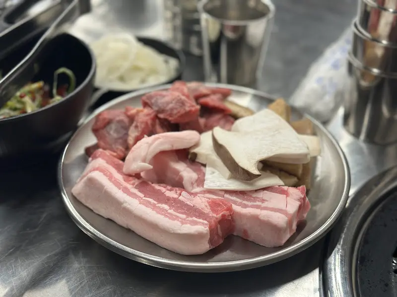 신선한 생삼겹살, 갈매기살, 버섯이 담긴 접시