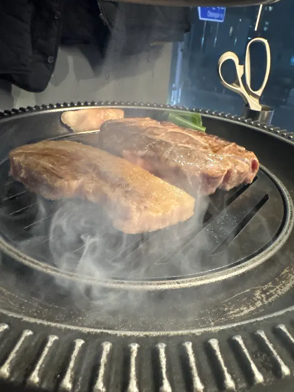 연기가 피어오르는 불판 위에서 두툼한 돼지고기가 구워지고 있는 모습