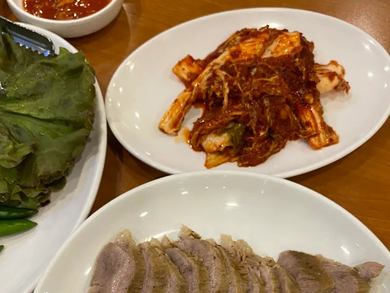 수육, 김치, 쌈 채소, 쌈장, 고추 등이 정갈하게 담겨 있는 모습