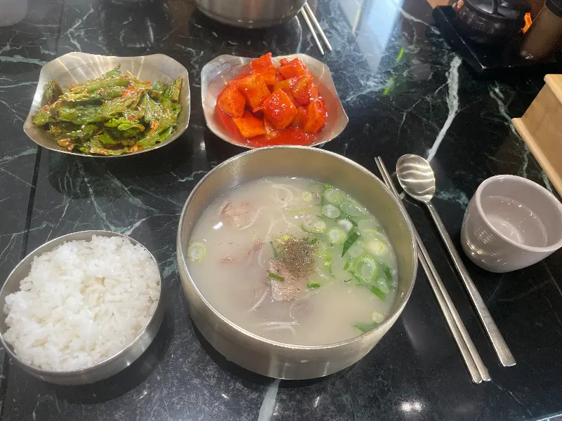 테이블 위에 설렁탕과 깍두기, 겉절이가 놓여있고, 밥그릇에는 밥이 담겨 있다.