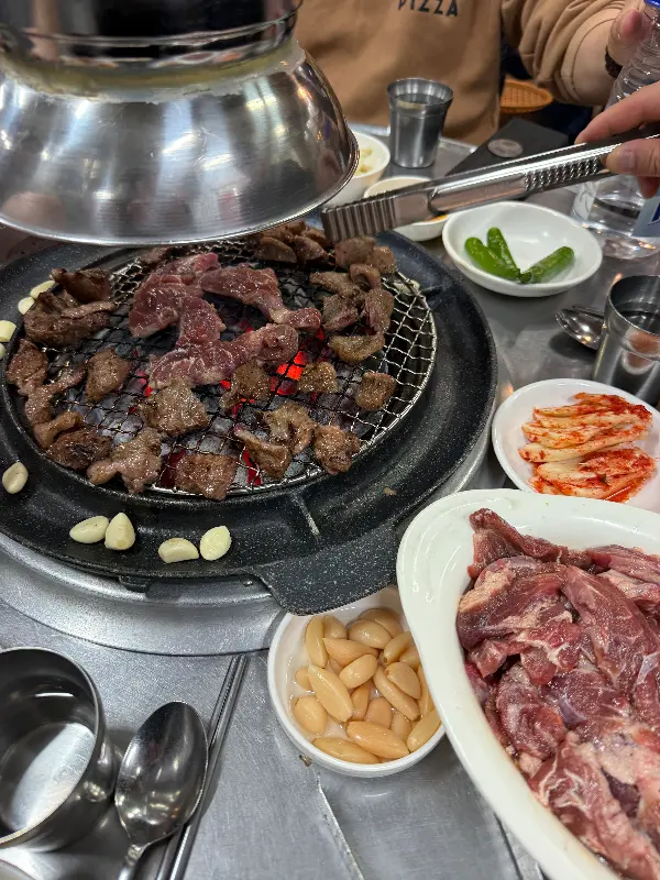 숯불 위에서 익어가는 갈매기살과 주변에 놓인 마늘, 김치