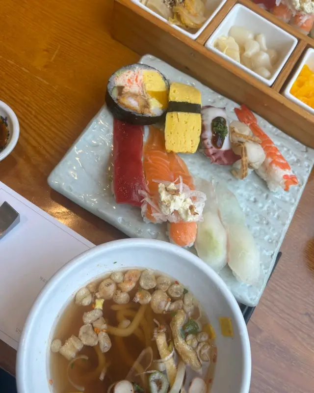 초밥, 우동, 튀김, 곁들임 반찬이 한 상 가득 차려진 모습