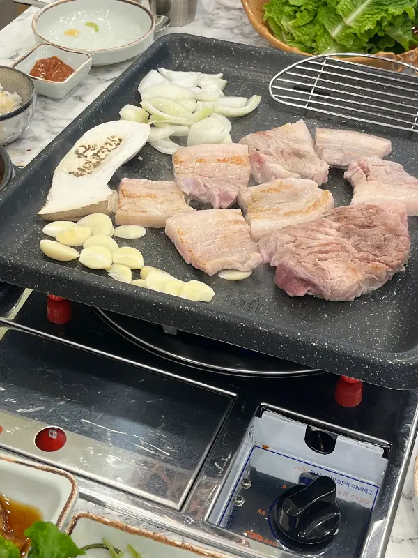 불판 위에 삼겹살, 양파, 버섯, 마늘이 함께 구워지고 있다.