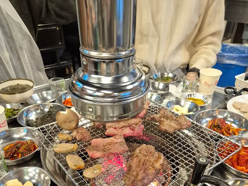 숯불 위에서 익어가는 고기와 주변에 놓인 다양한 밑반찬들