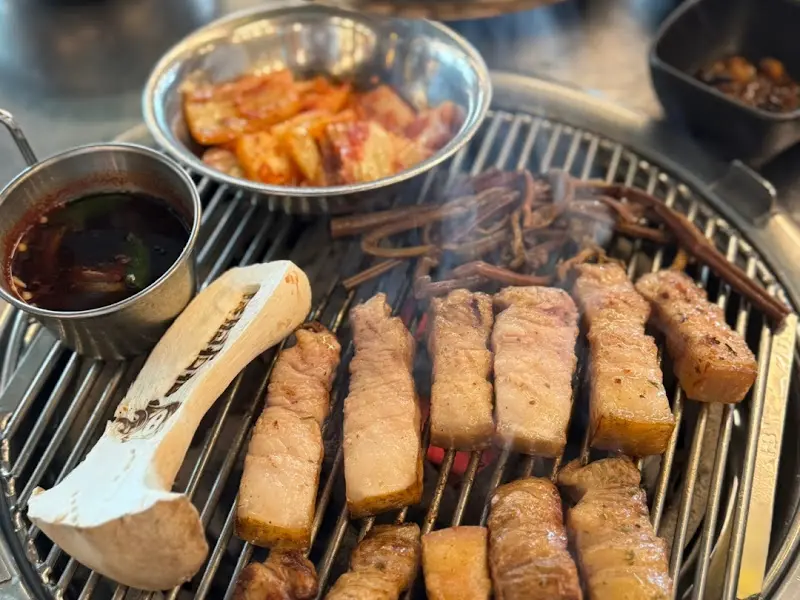 숯불 위에 올려진 흑돼지 오겹살과 김치, 멜젓의 모습. 지글거리는 소리가 들리는 듯하다.