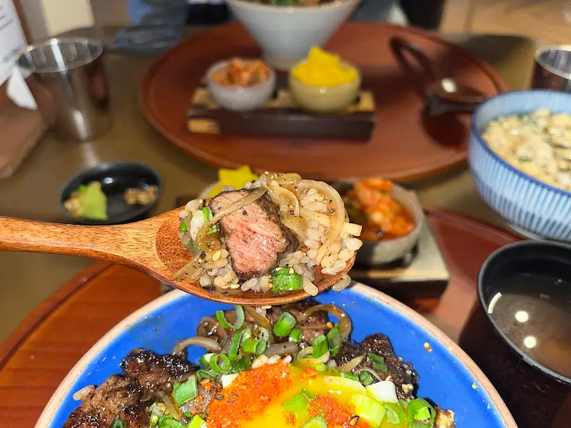 만코구의 스테이크 덮밥을 나무 스푼으로 떠먹는 모습