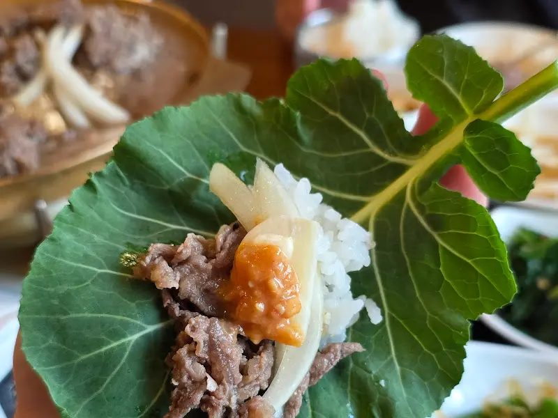 불고기, 밥, 버섯, 쌈장을 쌈에 싸서 먹는 모습