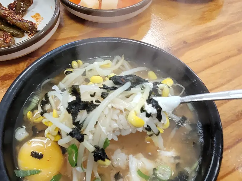 숟가락으로 콩나물 국밥을 뜨는 모습