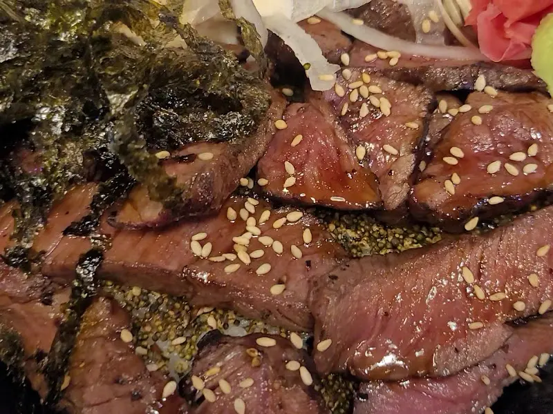 스테이크 덮밥 클로즈업 사진. 윤기가 흐르는 스테이크와 깨, 김 가루가 덮밥 위에 올려져 있다.