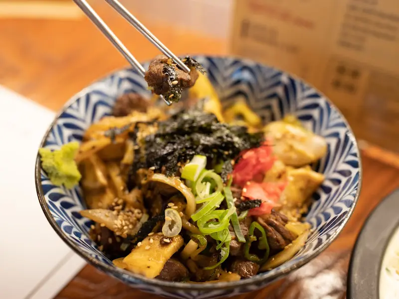 젓가락으로 스테이크를 집어 올린 사진. 윤기가 흐르는 스테이크가 맛있어 보인다.