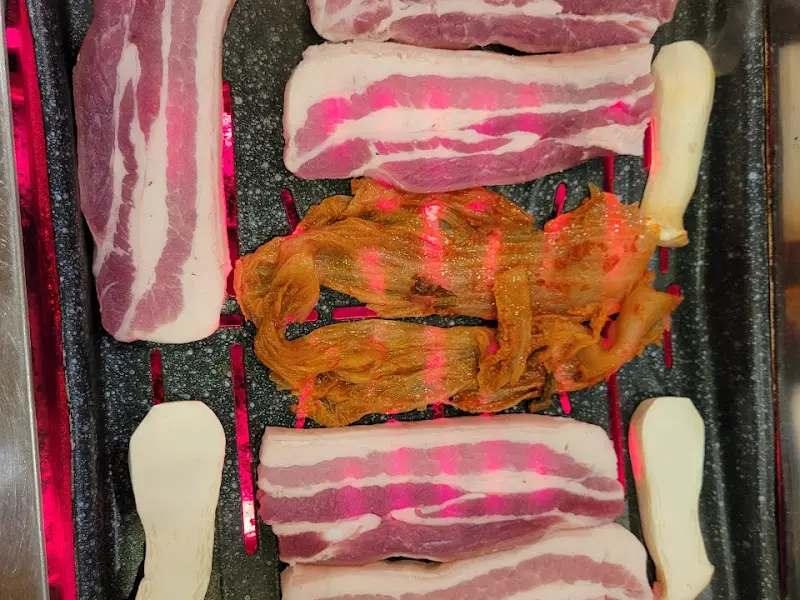 불판 위에서 맛있게 익어가는 삼겹살과 김치, 버섯