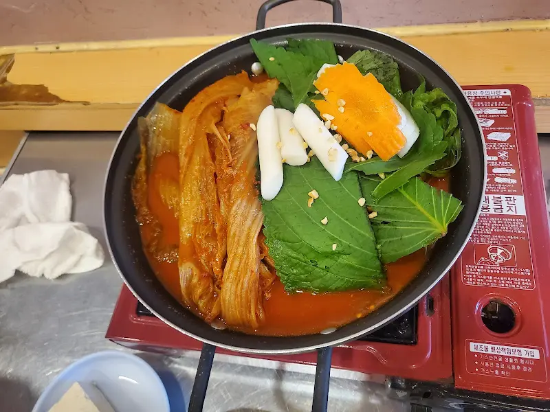 매운 등갈비찜이 빨간 양념에 버무려져 김치, 떡, 깻잎과 함께 냄비에 담겨 있다.