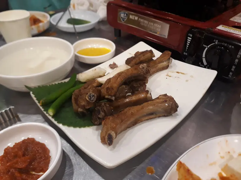 쪽갈비 구이가 흰색 접시에 담겨 나온 모습. 옆에는 소스와 야채가 함께 있다.