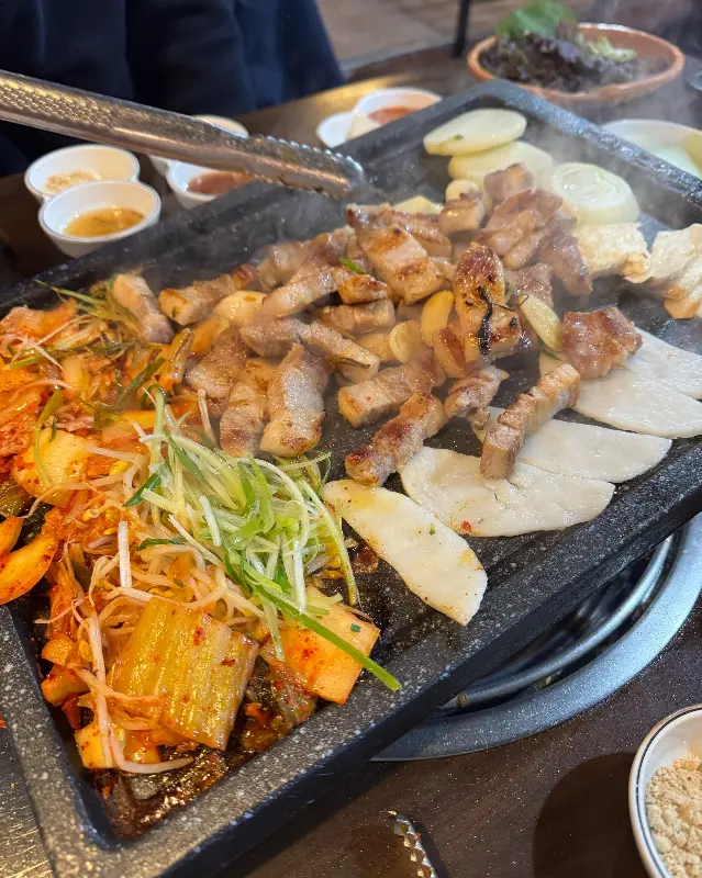 돌판 위에 가득찬 삼겹살, 김치, 떡, 두부