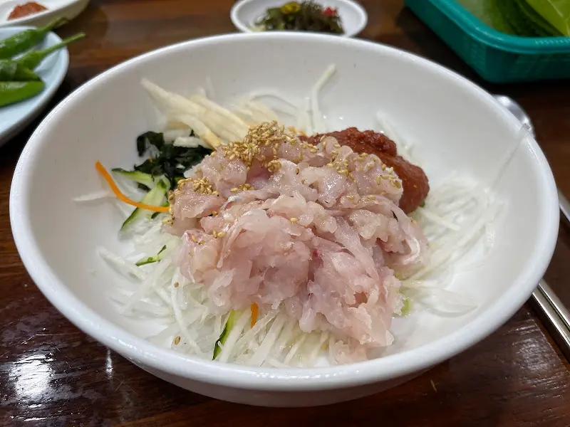 윤기가 흐르는 아까무스 물회의 클로즈업 사진. 붉은 양념장과 신선한 채소가 조화롭게 담겨 있다.