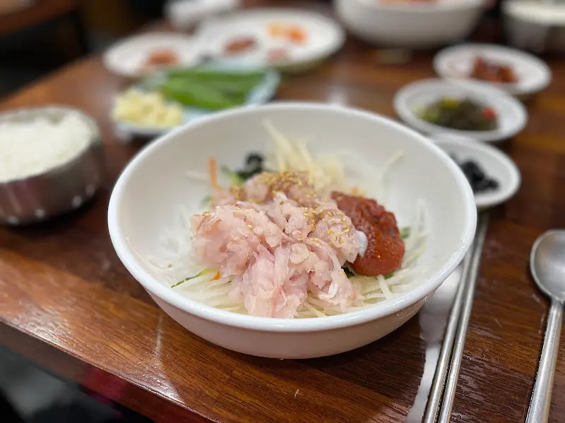 테이블 위에 놓인 물회, 밥, 밑반찬, 매운탕의 전체적인 모습.