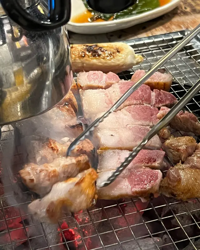 잘 구워진 오겹살 한 점을 젓가락으로 집어 올리는 모습