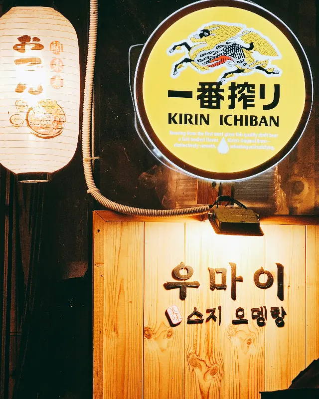 따뜻한 조명 아래 나무 간판에 쓰인 '우마이'라는 상호명