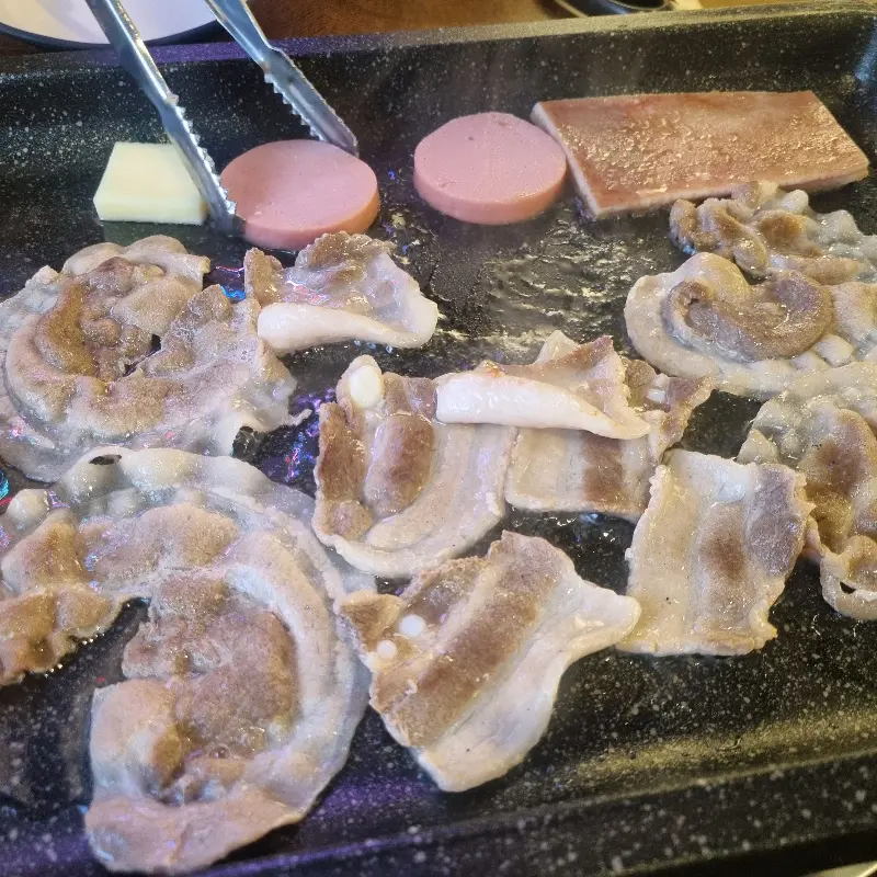 불판 위에서 지글거리는 냉꽃삼겹, 소시지, 치즈