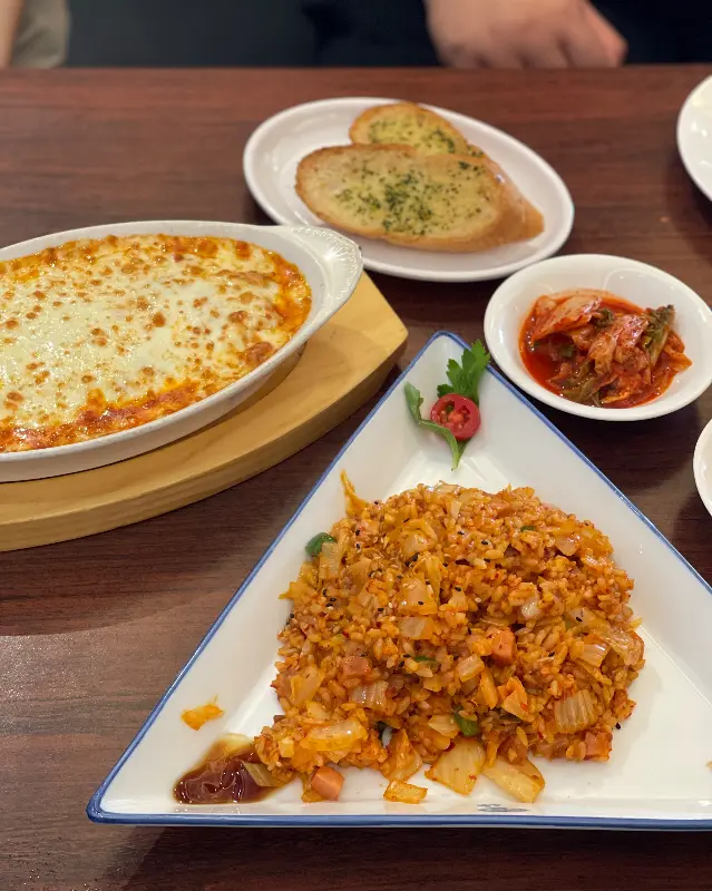 김치볶음밥, 치즈오븐스파게티, 마늘빵이 함께 놓인 테이블 사진