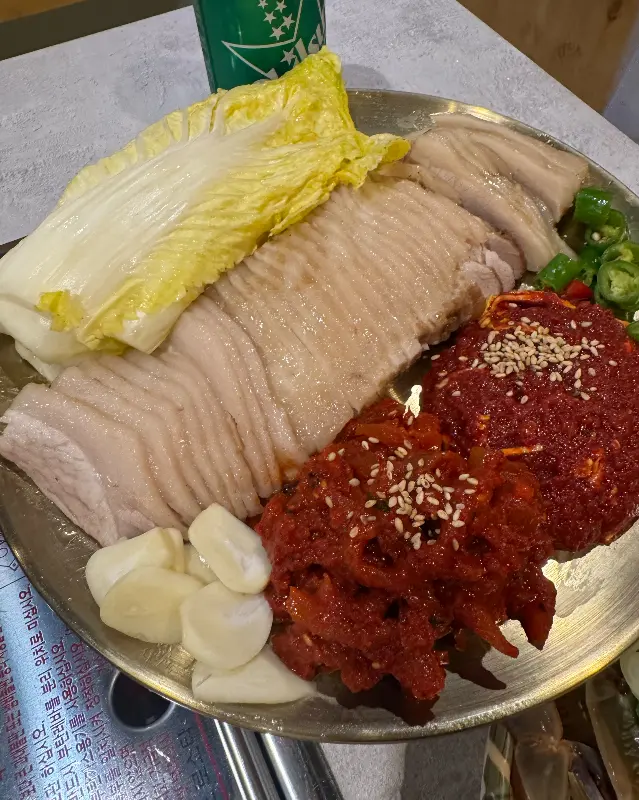 잘 삶아진 가브리살 수육과 김치, 배추, 마늘이 담긴 접시