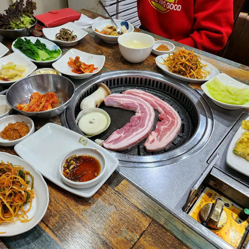 숯불 위에 올려진 흑돼지 오겹살과 푸짐한 밑반찬