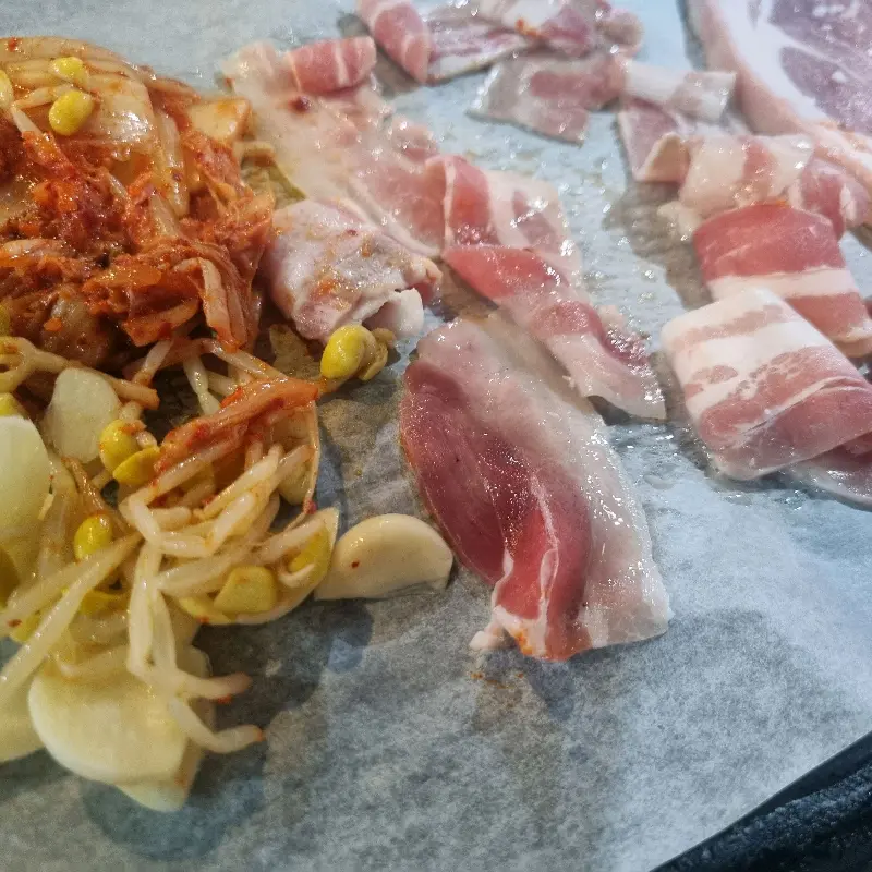 불판 위에서 익어가는 삼겹살과 김치, 콩나물의 조화