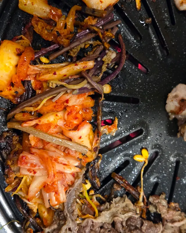 불판 위에서 구워진 김치와 콩나물, 고기